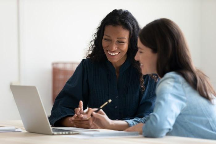 在会议上，快乐的年轻非裔美国女商人使用笔记本电脑和大笑的女导师. 面带微笑的多元化女经理们在谈论新的经营理念.