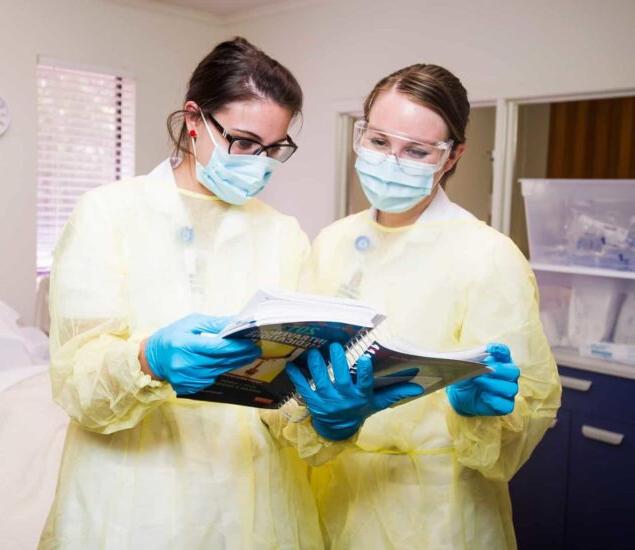 Nurses with personal protective equipment studying a book.