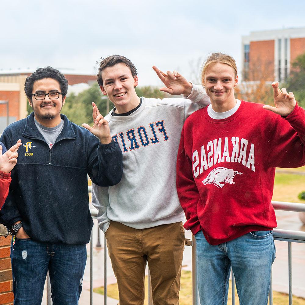 Three students wearing pullovers from other universities.